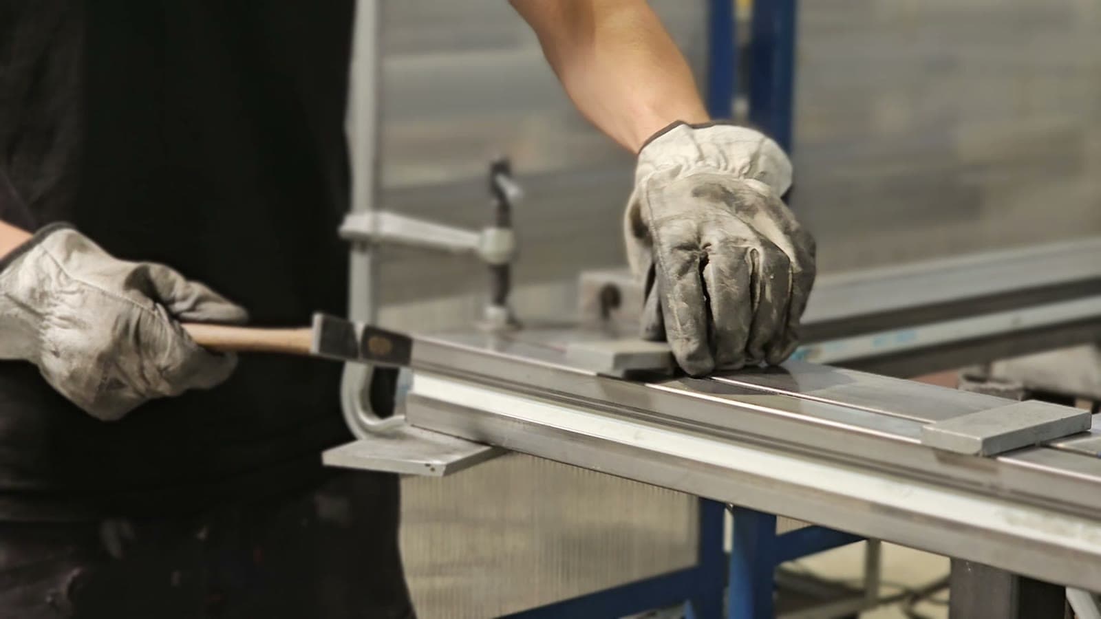 Mains gantées ajustant au marteau et au serre-joint un profilé aluminium sur l'établi