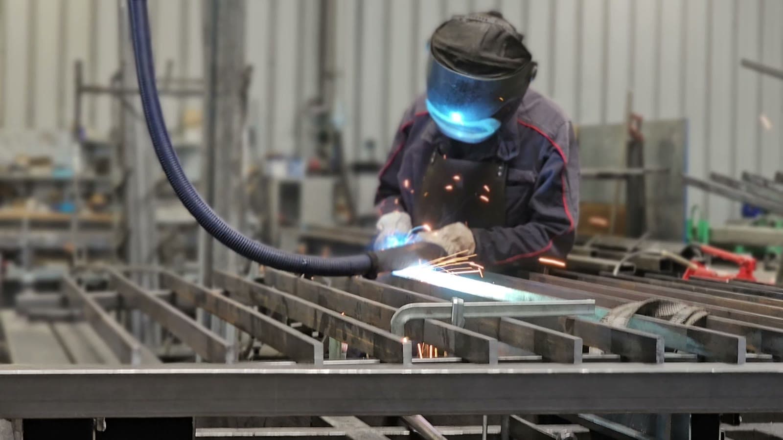 Soudeur à l'arc assemblant un châssis acier dans l'atelier Distrifermetures, gerbe d'étincelles